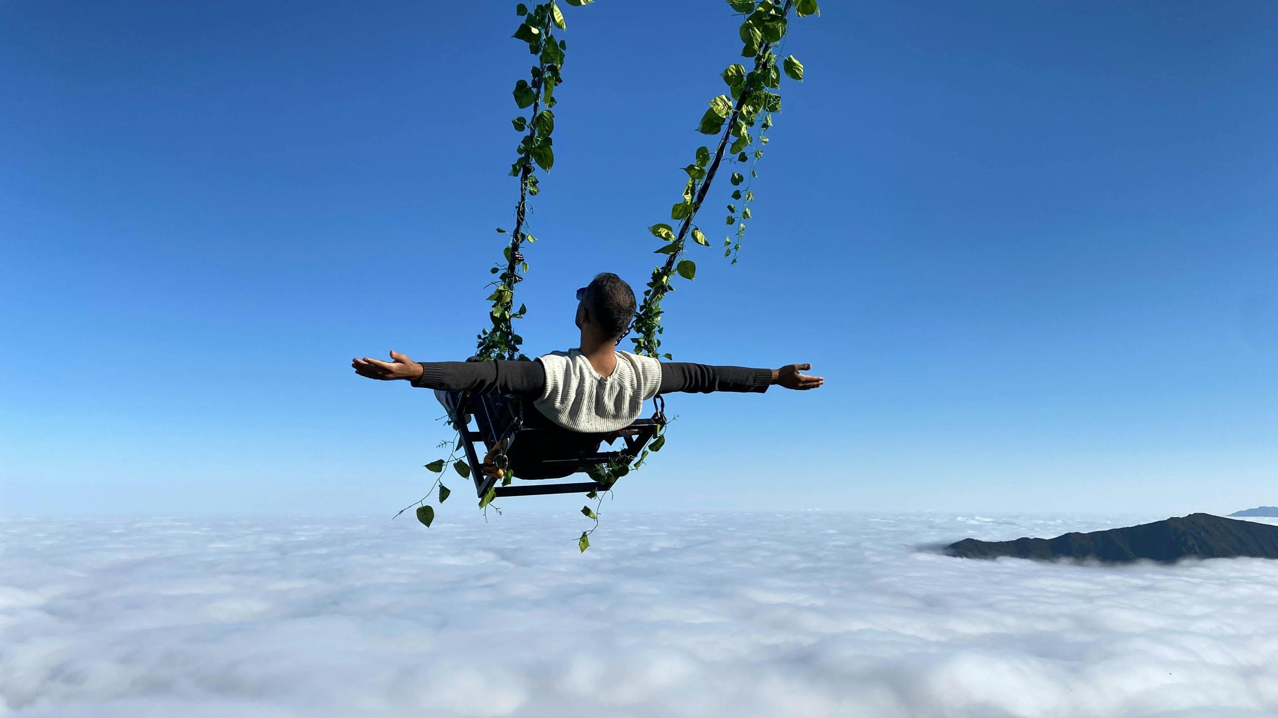 A man swings over a vast sea of clouds, arms wide open, embracing the thrill and serenity of nature.