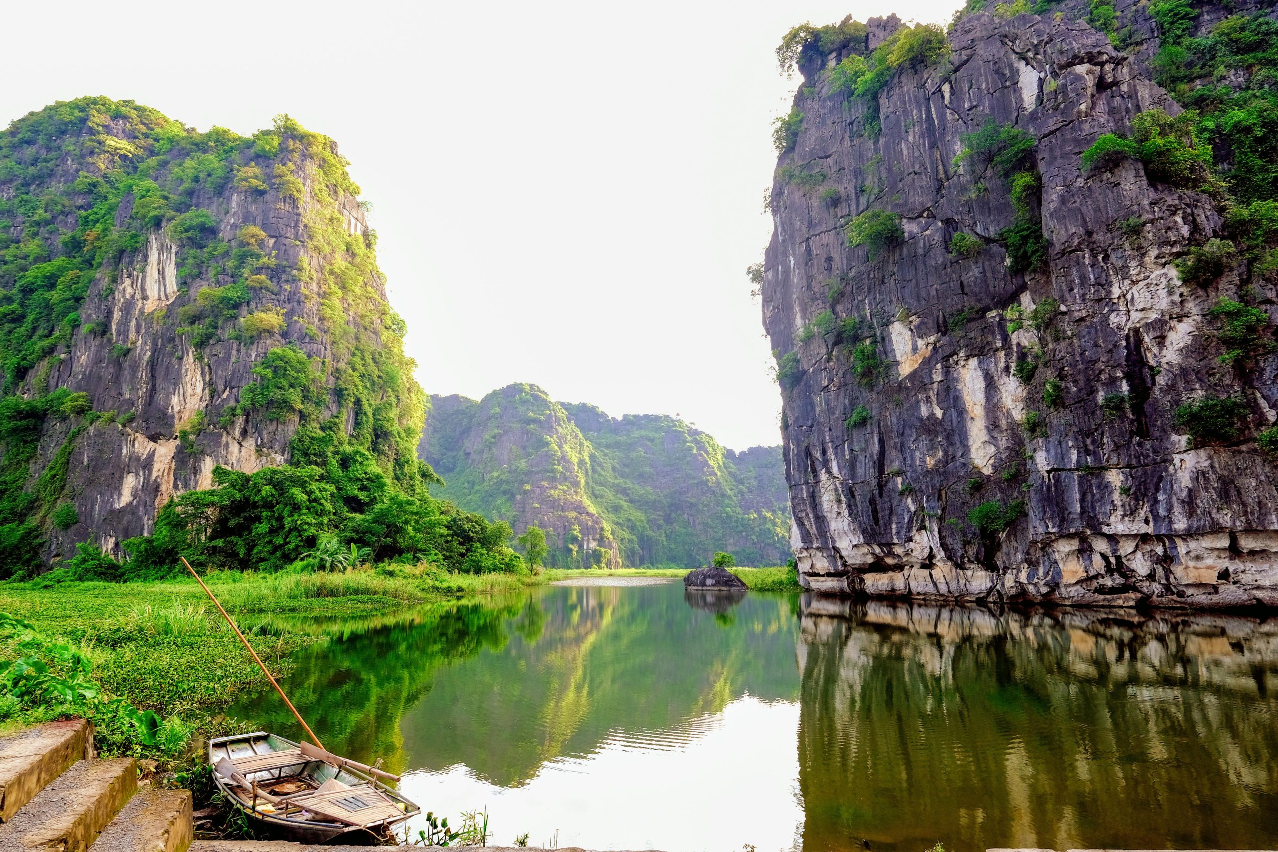 Tranquil scene of Ninh Binh's limestone cliffs and serene water reflection, featuring a traditional rowboat.