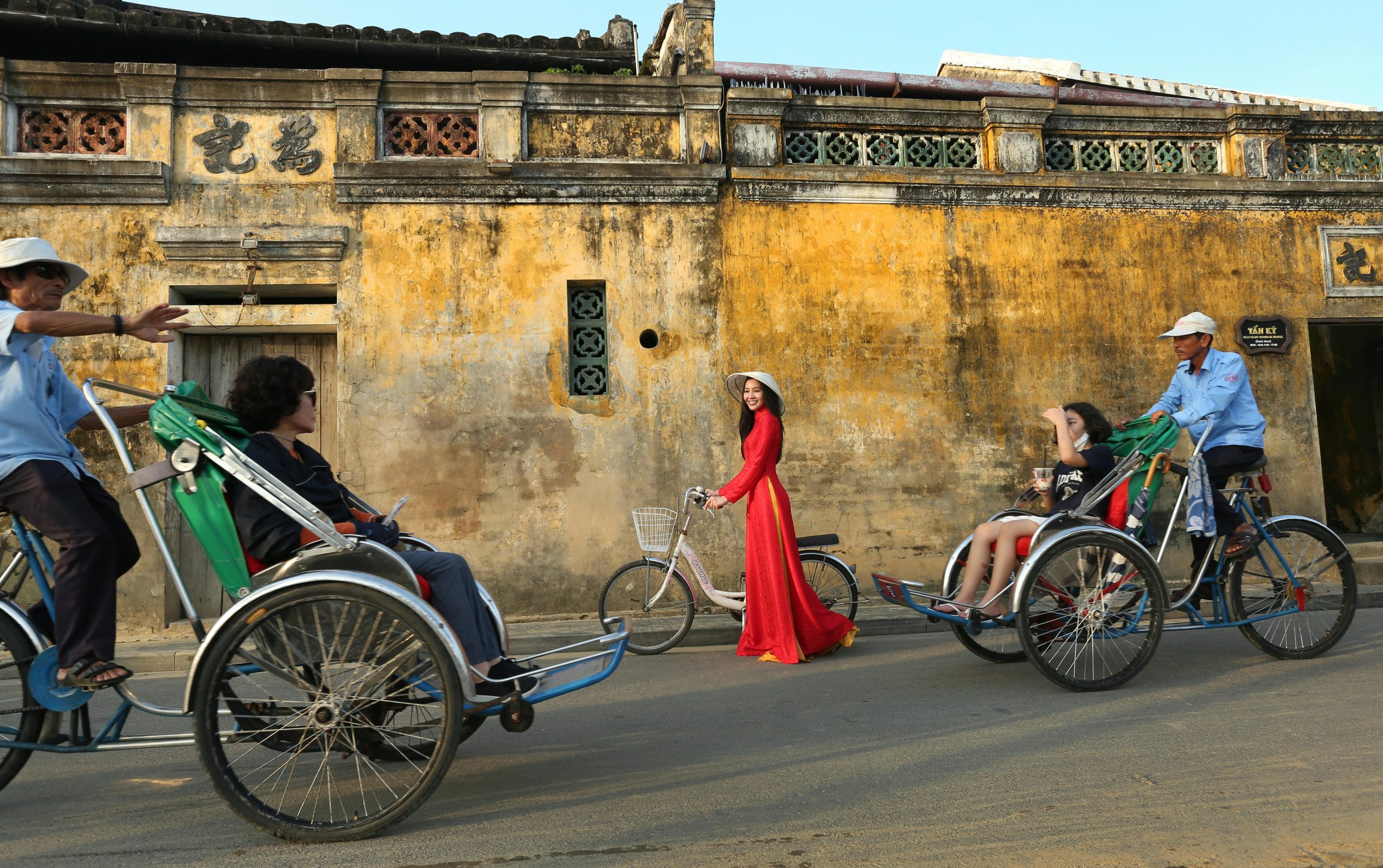 Colorful street scene in Hoi An, Vietnam featuring a woman in Ao Dai and cyclos.